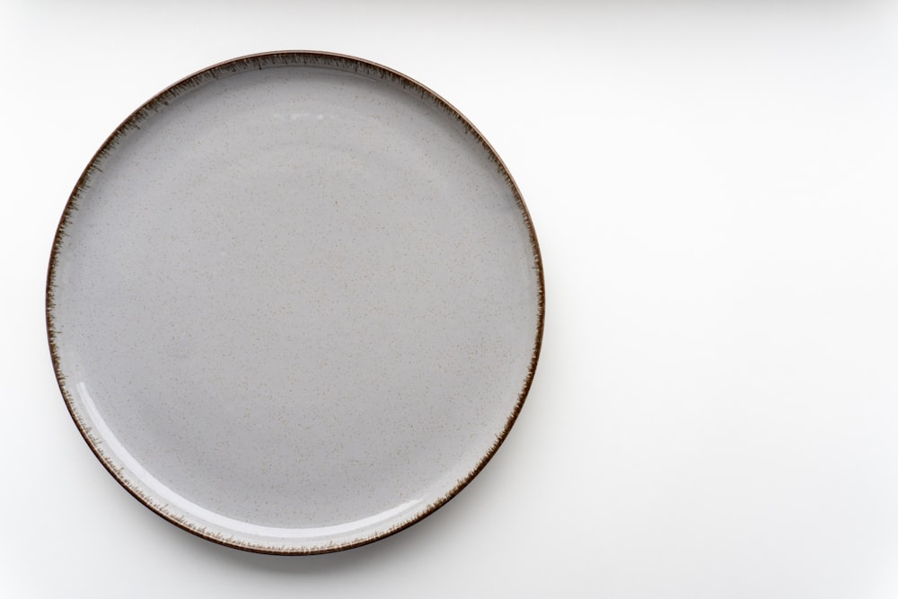 a white plate with a brown rim on a white surface