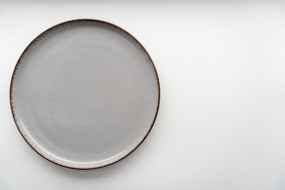 a white plate with a brown rim on a white surface