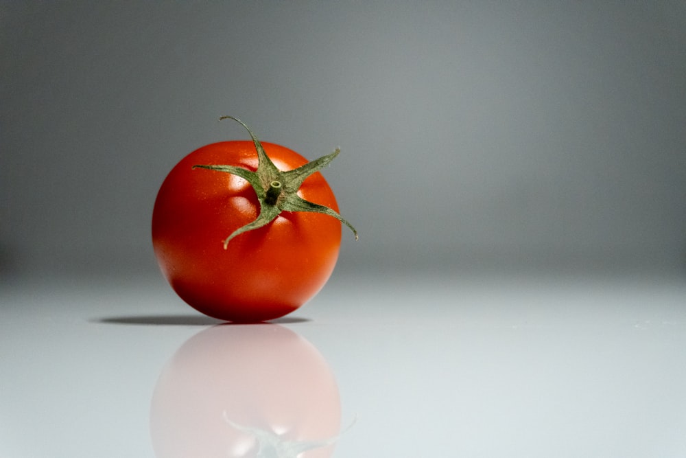 a single tomato sitting on a reflective surface
