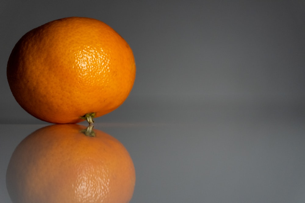an orange sitting on top of a reflective surface