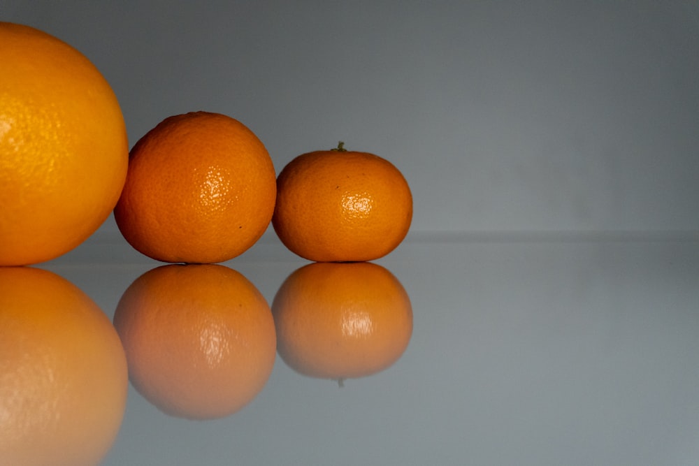 three oranges sitting on top of a reflective surface