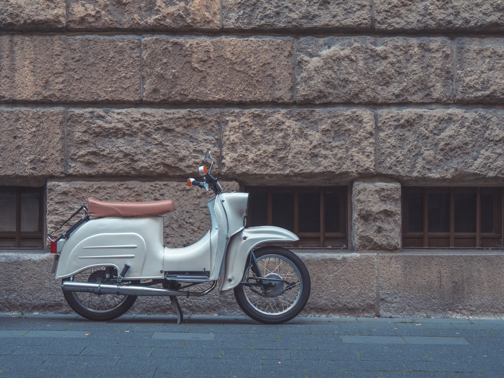 a white scooter parked next to a stone wall