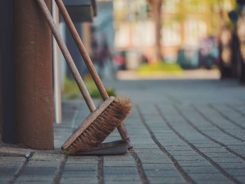 a broom leaning against a pole on a sidewalk