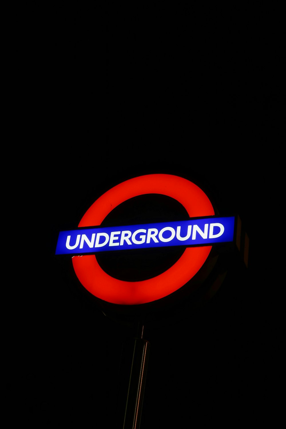 a red and blue underground sign lit up at night