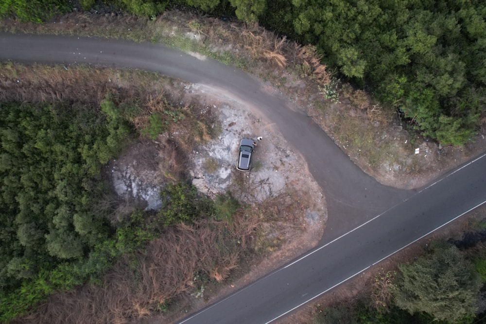 an aerial view of a car parked on a road in the middle of a forest
