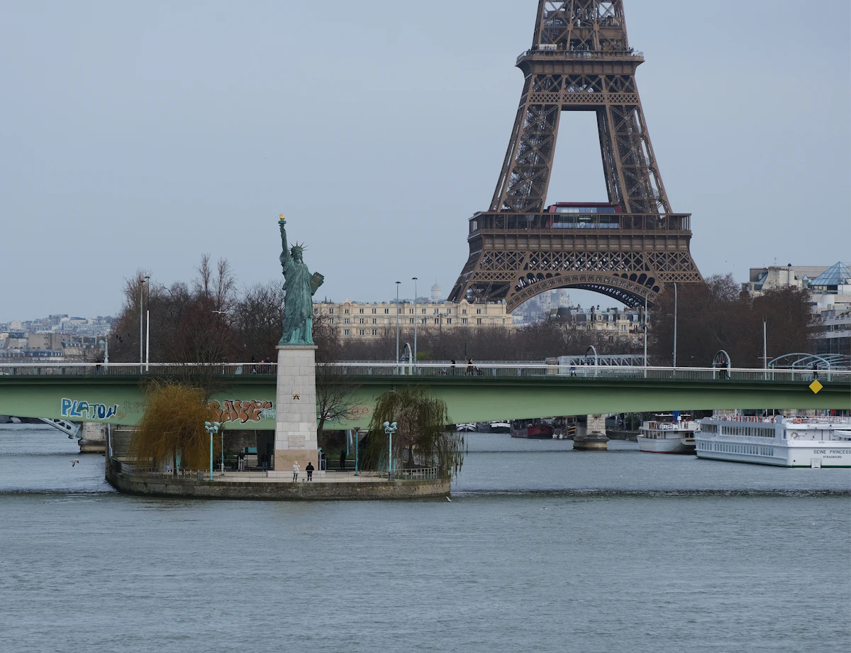 The Statue of Liberty replica on the Île aux Cygnes, in front of a bridge over the Seine and the Eiffel Tower