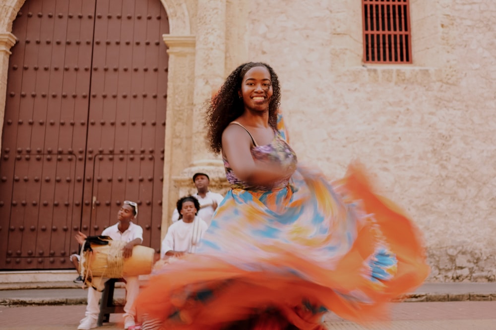 uma mulher em um vestido colorido dançando na frente de um grupo de pessoas