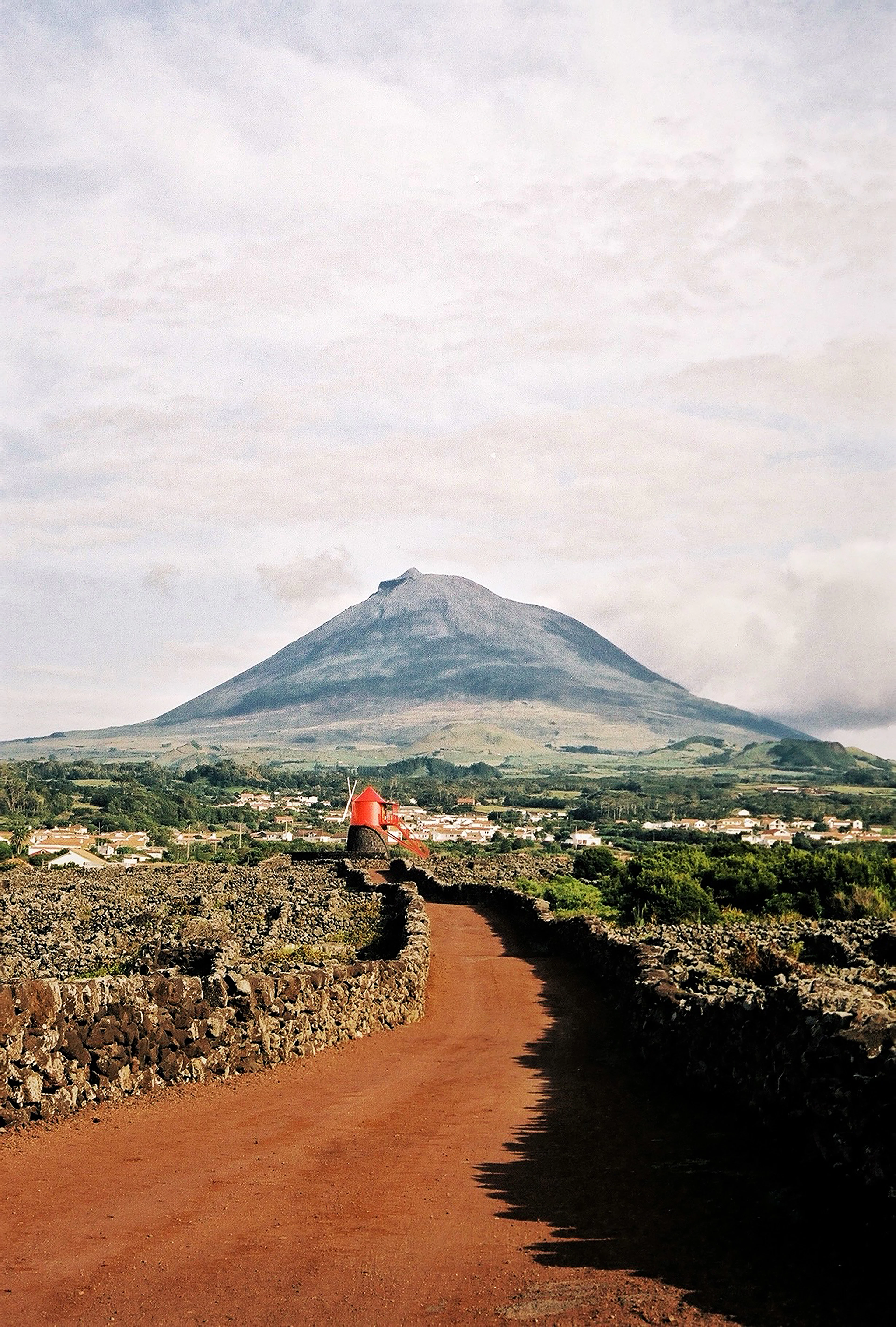 The cone of Mount Pico above lava-stone-walled vineyards and a red windmill on Pico island
