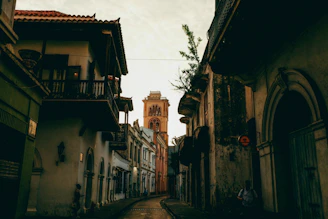 a narrow street with a clock tower in the background