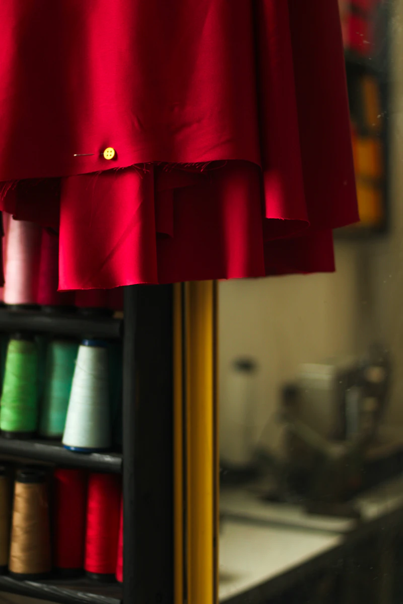 A red dress hanging on a rack beside spools of thread