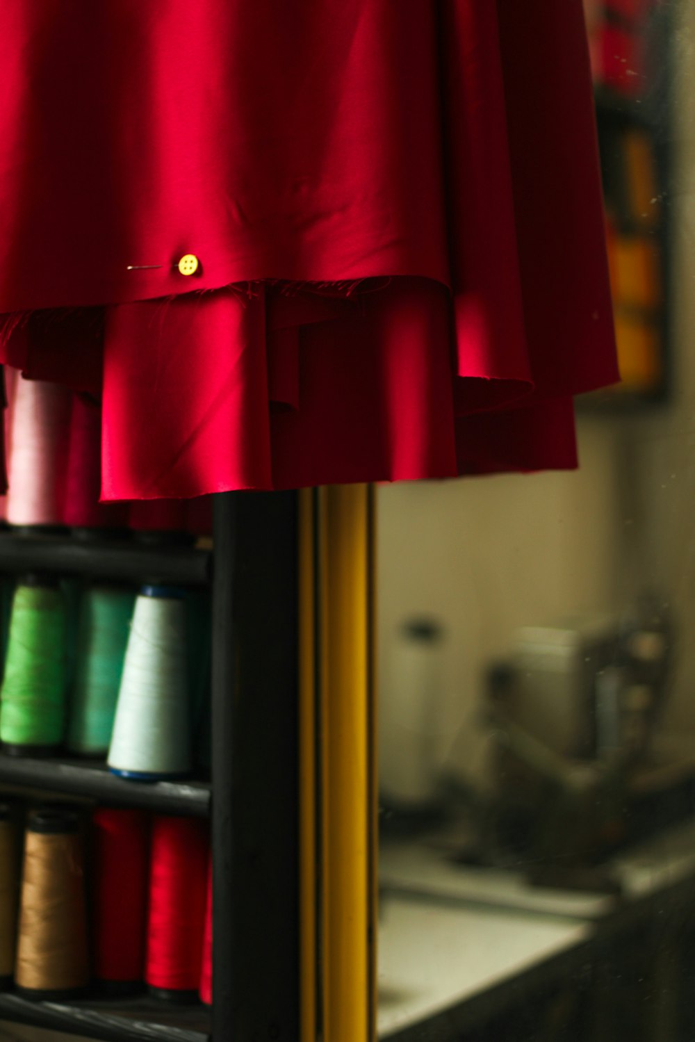 a red dress hanging on a rack with spools of thread