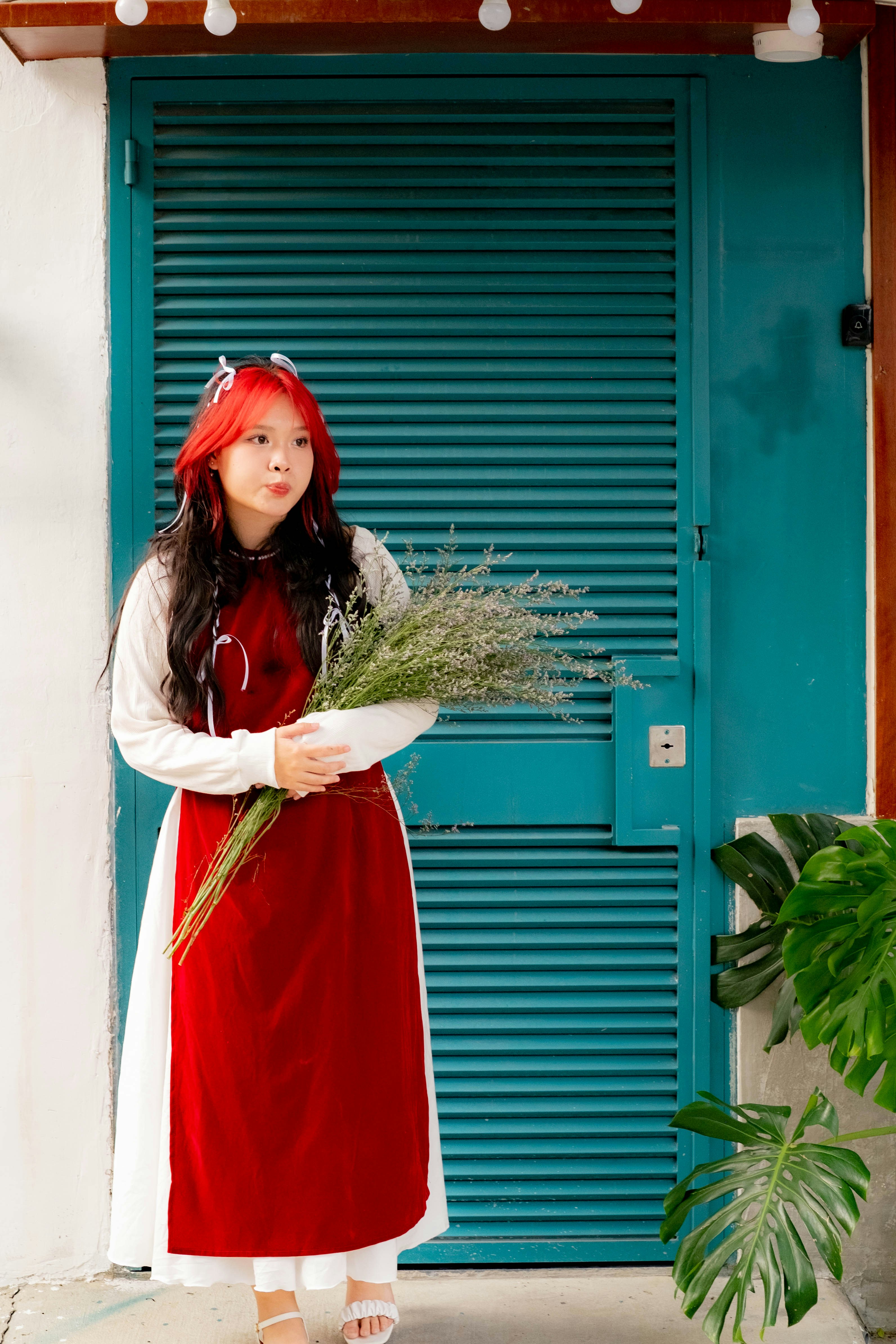 Seorang wanita dengan gaun merah dan putih memegang buket bunga
