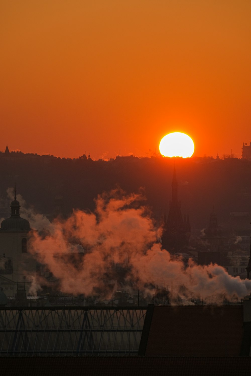 the sun is setting over a city with steam coming out of it