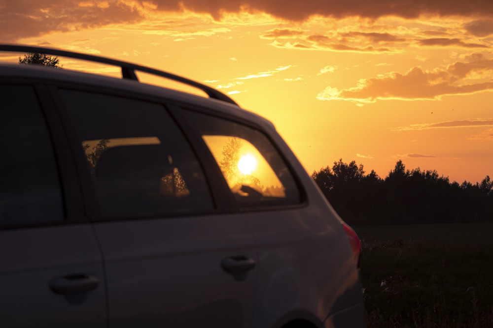 the sun is setting behind a car in a field