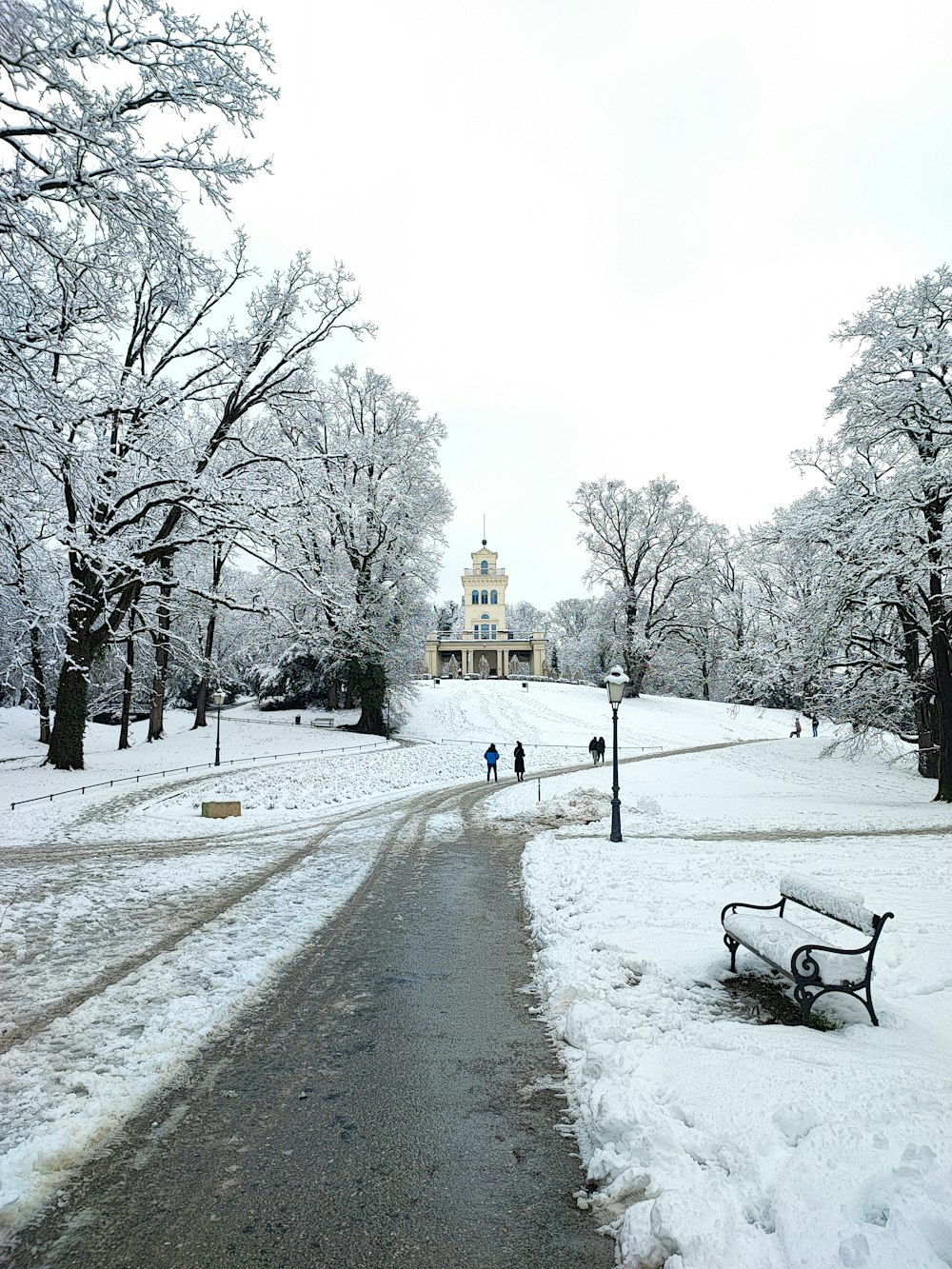 a park bench covered in snow next to a road