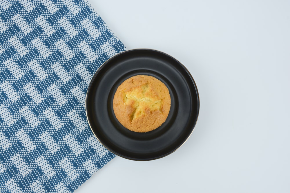 a muffin in a black plate on a blue and white cloth