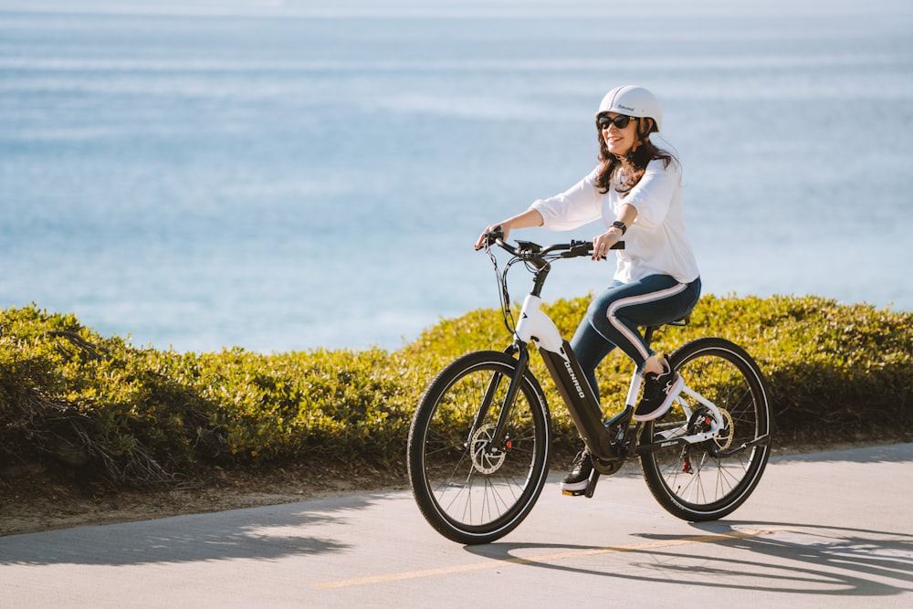 a woman riding a bike down a road next to the ocean