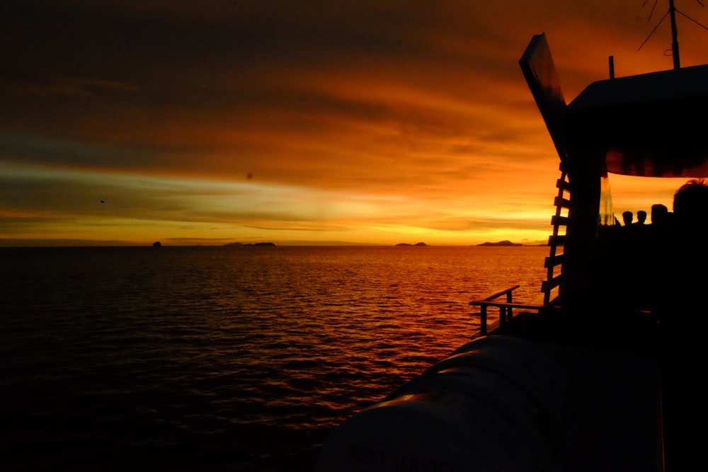 the sun is setting over the ocean with a boat in the foreground