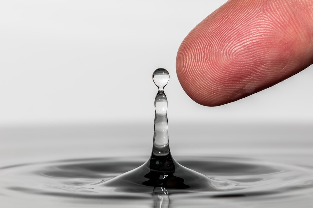 a finger touching the tip of a drop of water