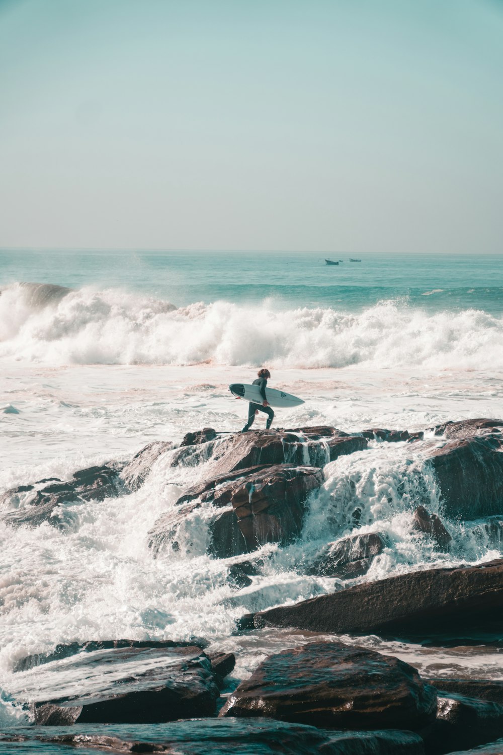 a man holding a surfboard standing on top of a rock