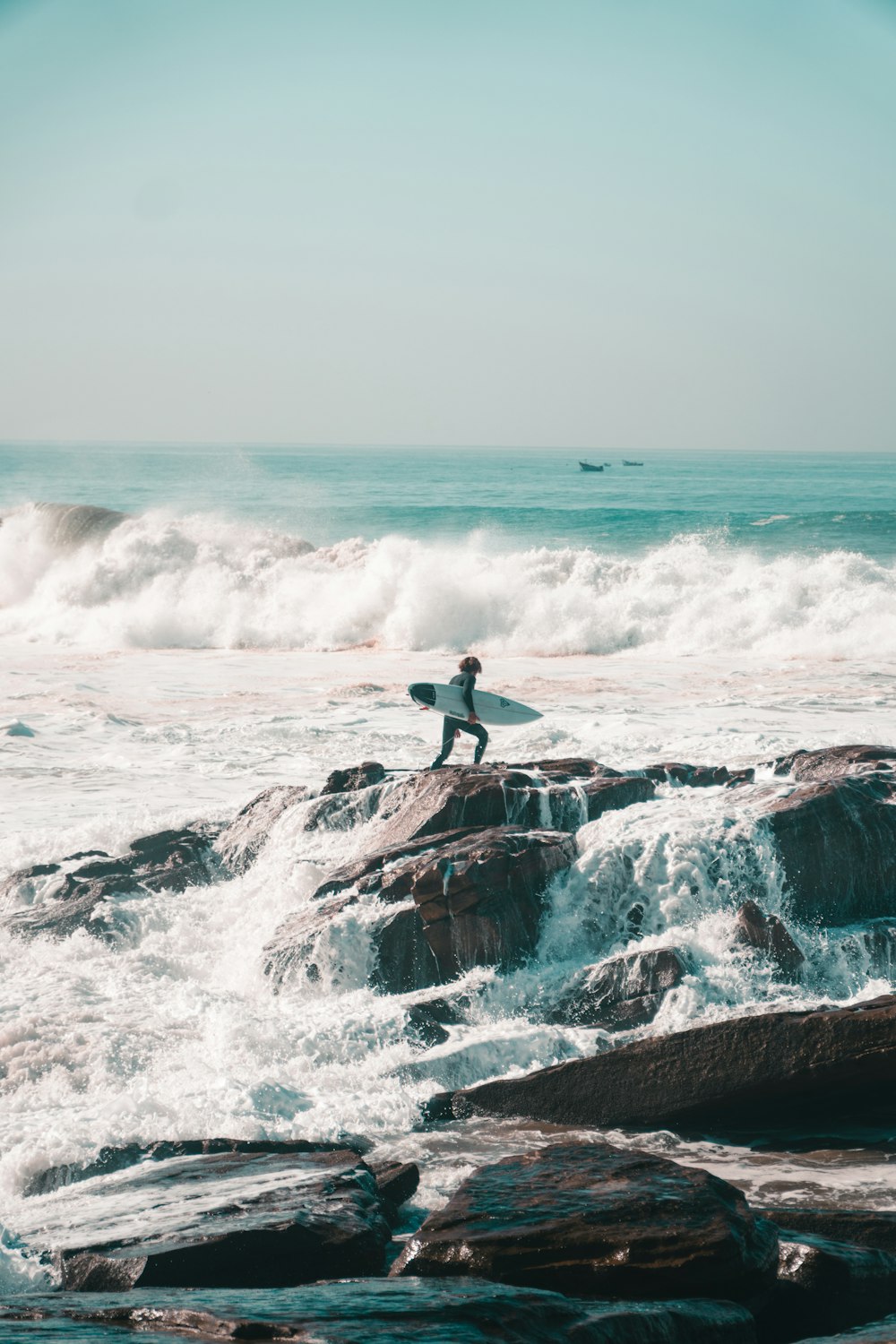 a man holding a surfboard standing on top of a rock