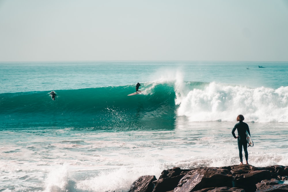 a person standing on a rock in front of a wave