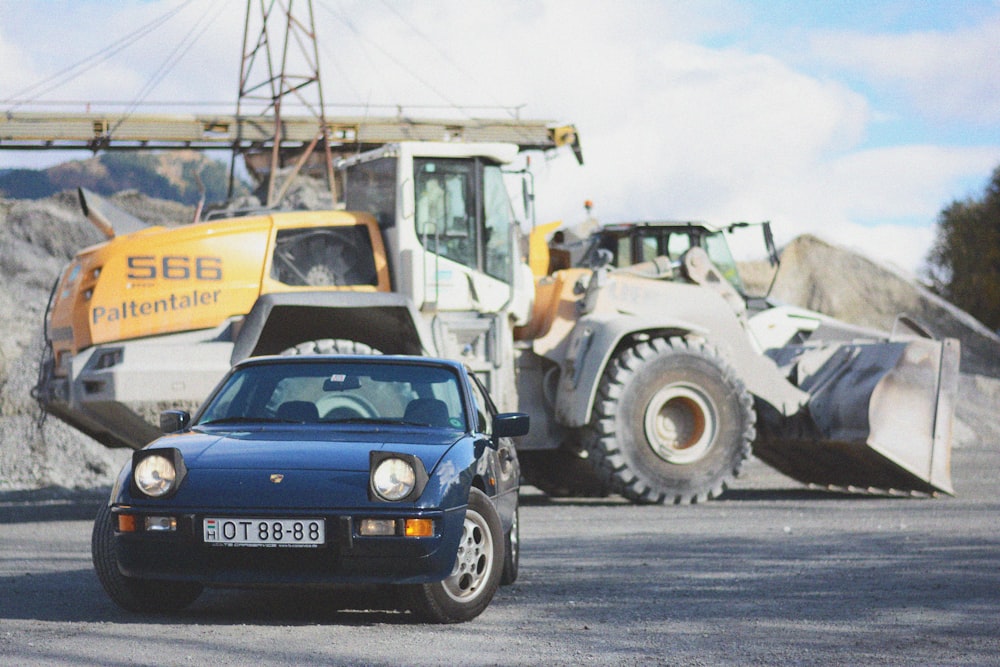 a blue car is parked in front of a bulldozer