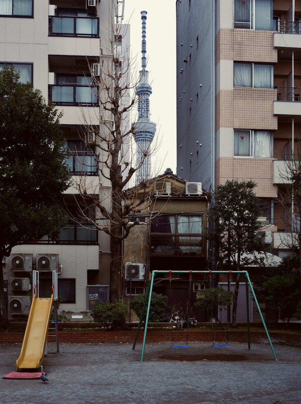 a playground with a yellow slide and a tall building in the background