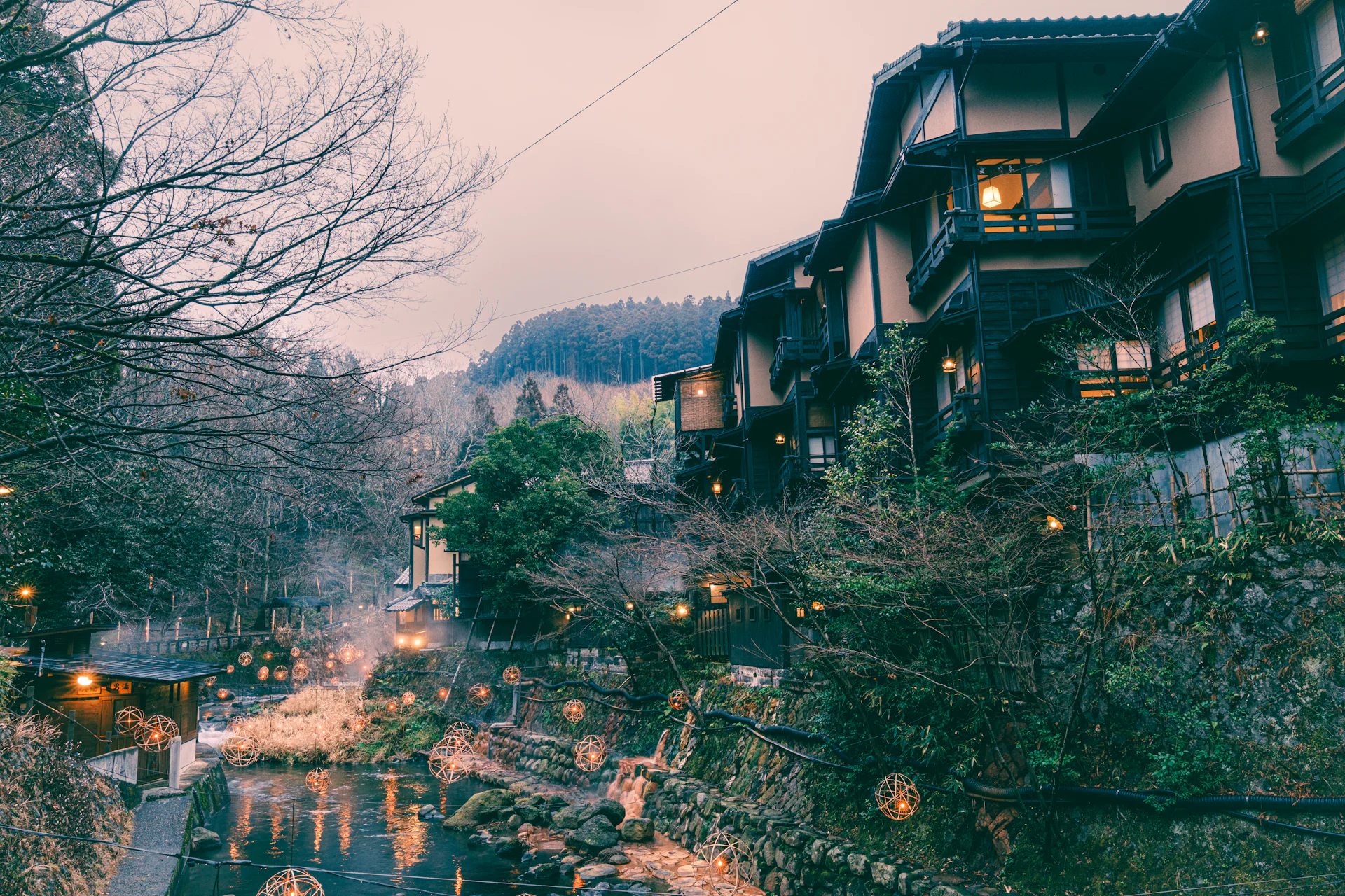 Wooden onsen inns above a river lit with lanterns at dusk
