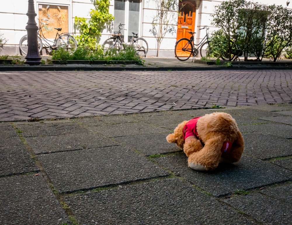 a brown teddy bear sitting on top of a sidewalk