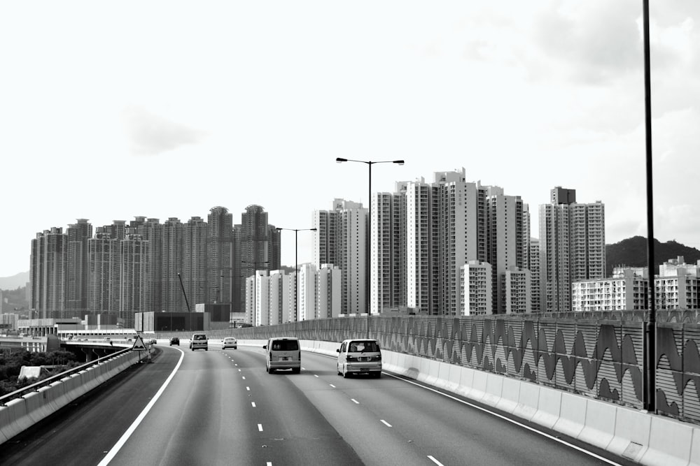 a black and white photo of a highway with buildings in the background
