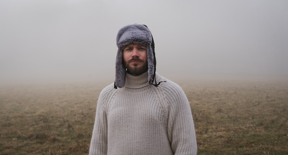 a man wearing a hat and sweater in a foggy field