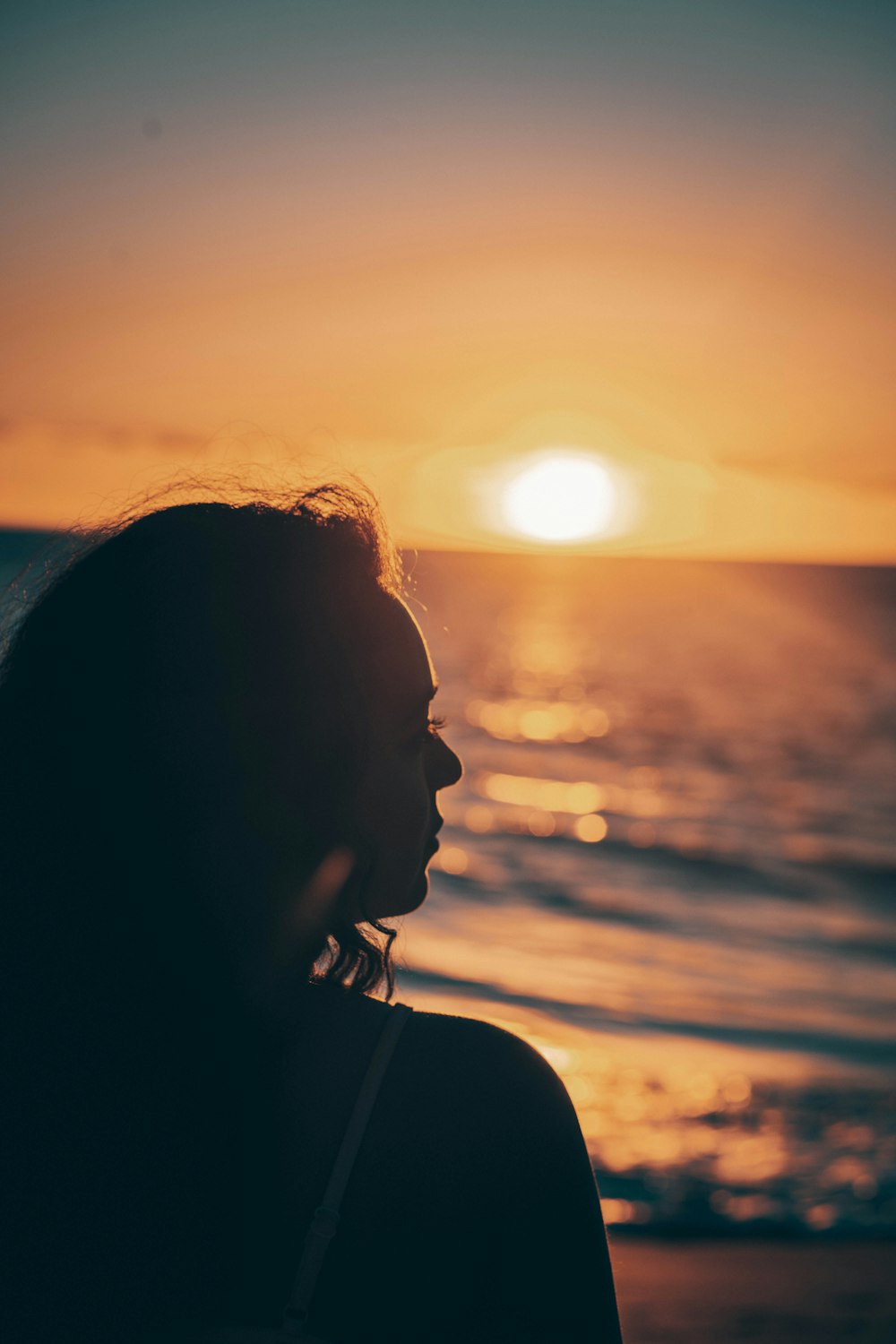 a woman standing in front of the ocean at sunset