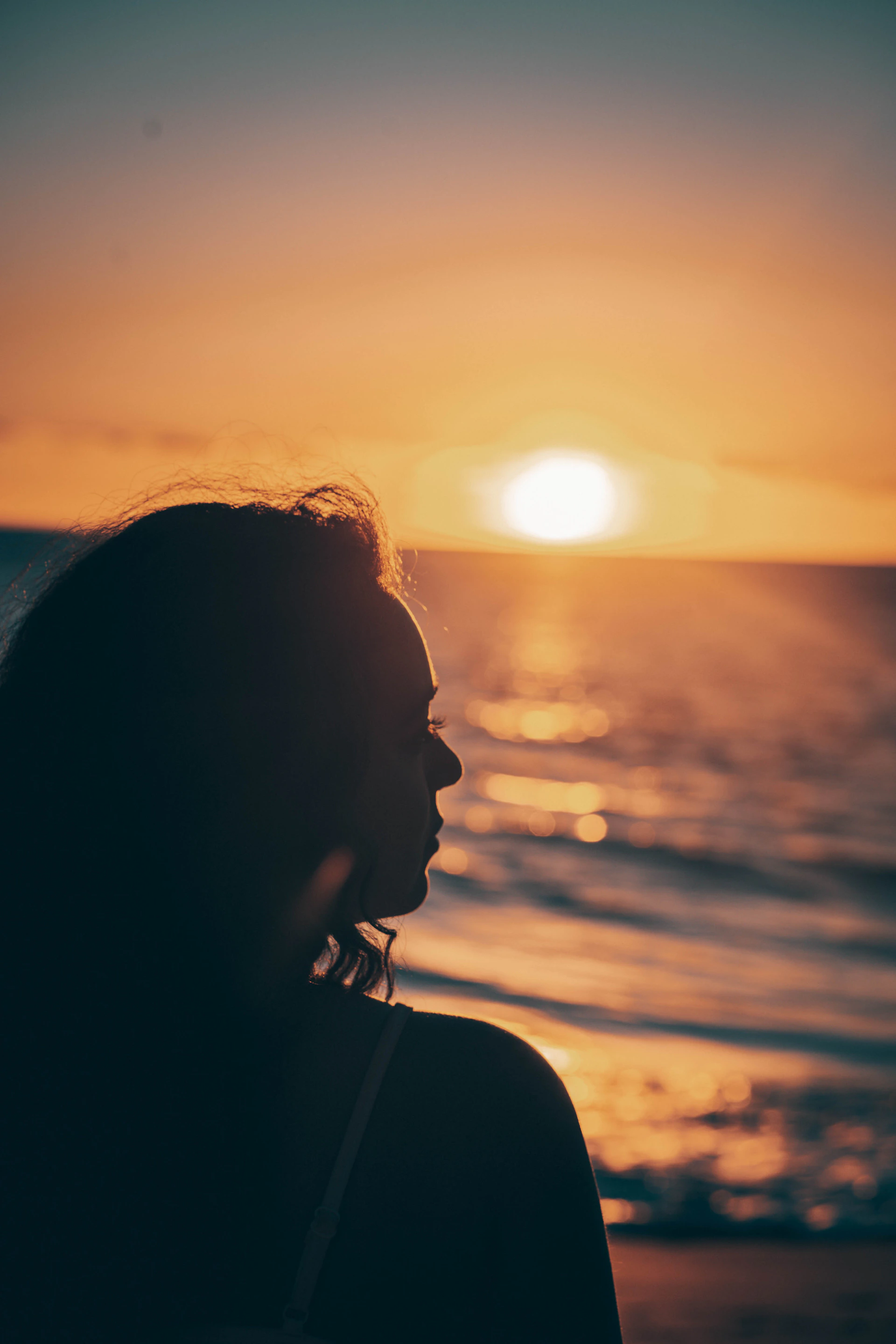 a woman standing in front of the ocean at sunset