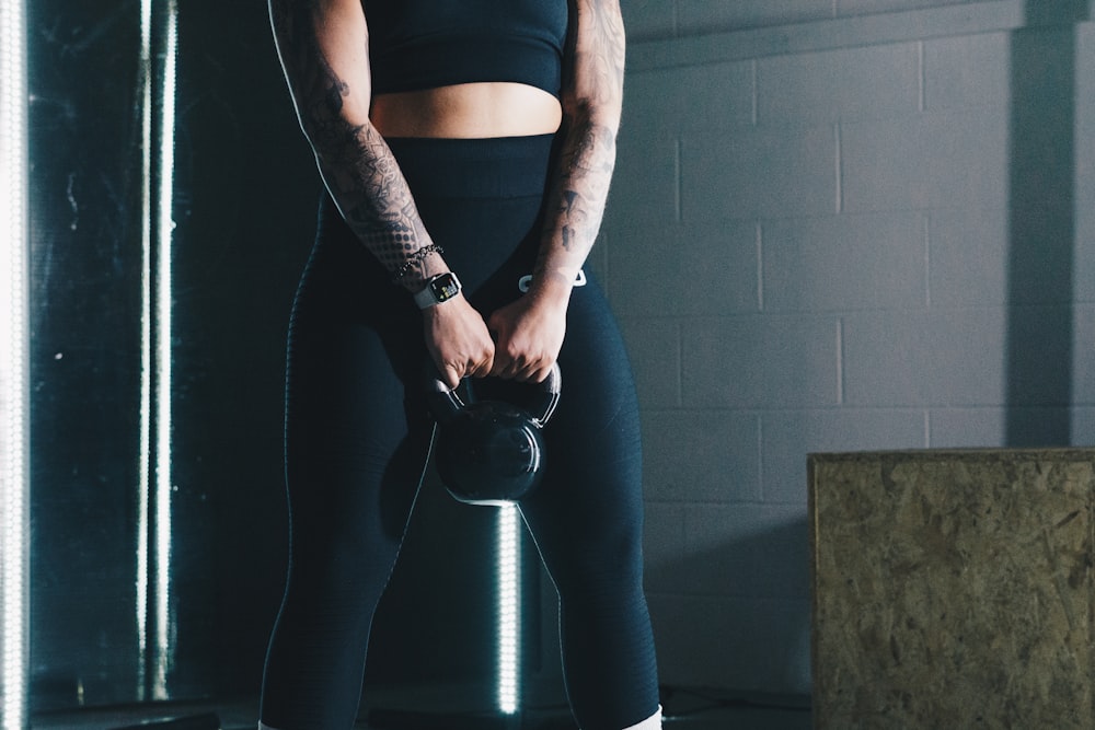 a woman with tattoos holding a kettle in a gym