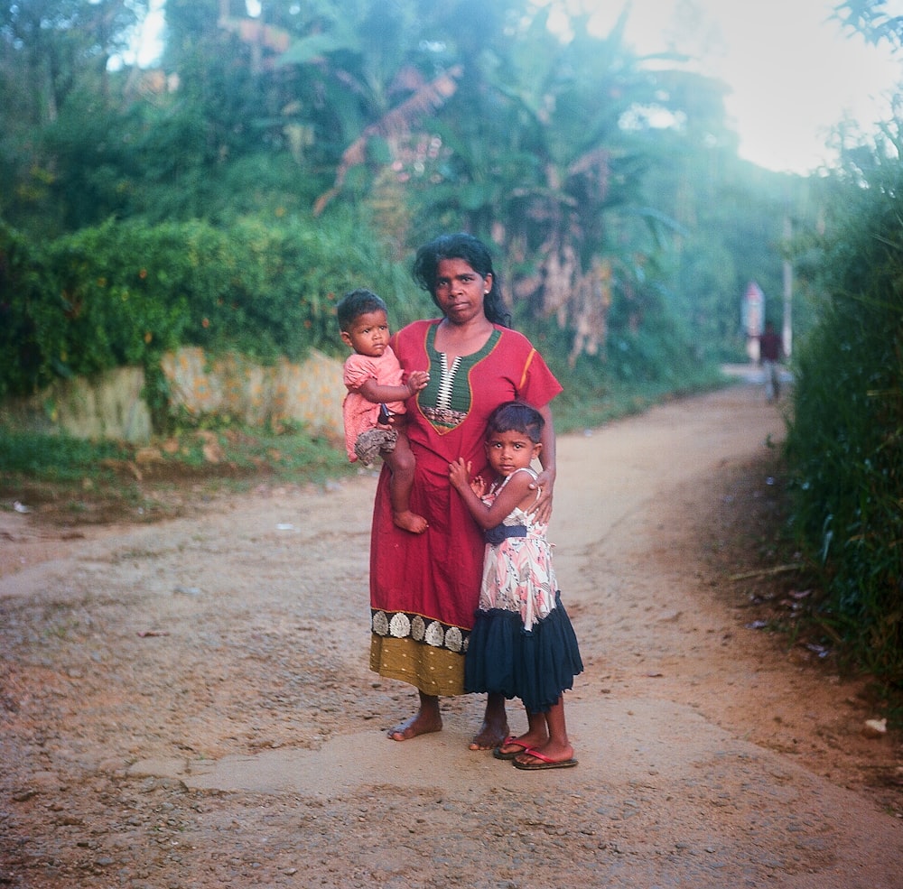 a woman and two children standing on a dirt road