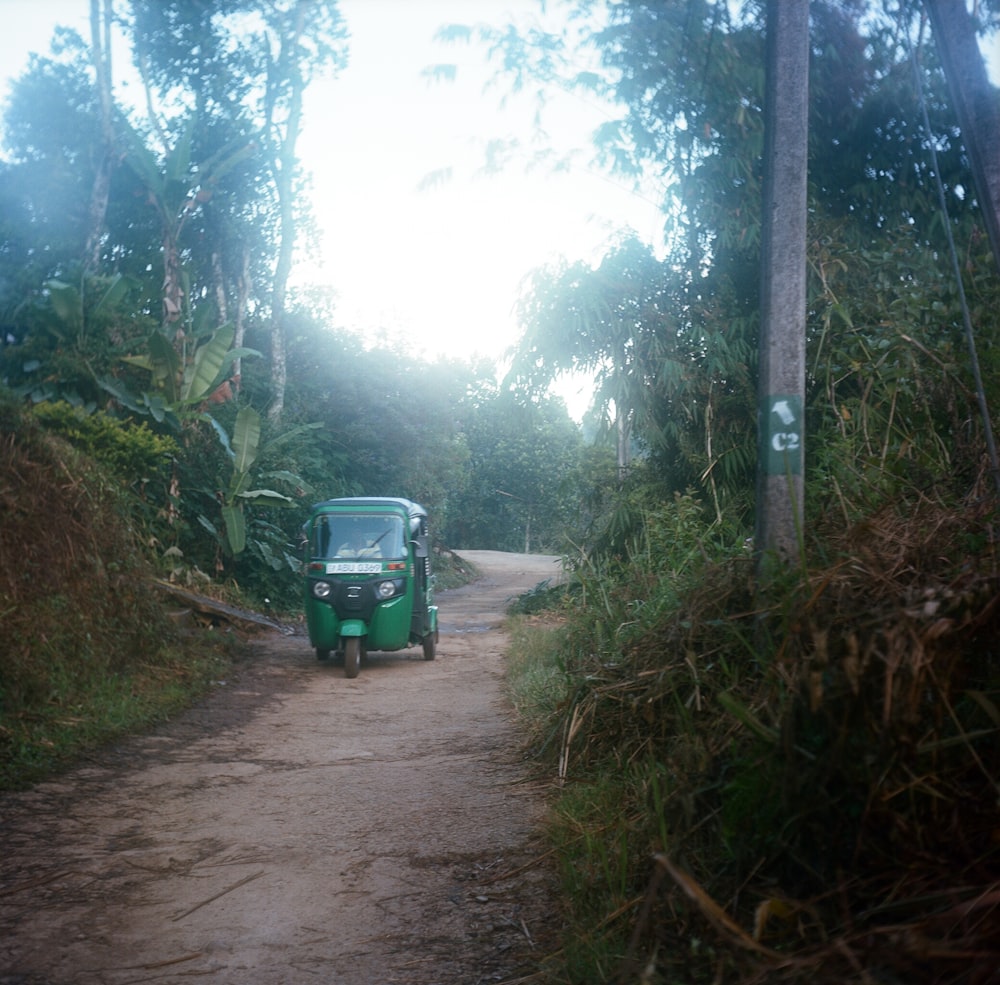 a small green truck driving down a dirt road