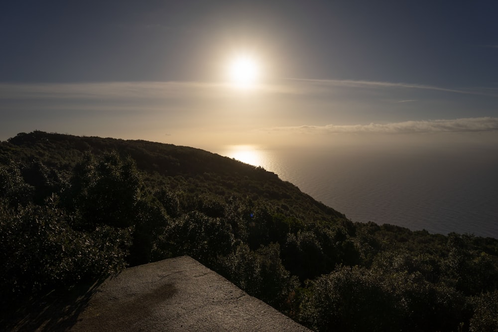 the sun is setting over the ocean on a hill