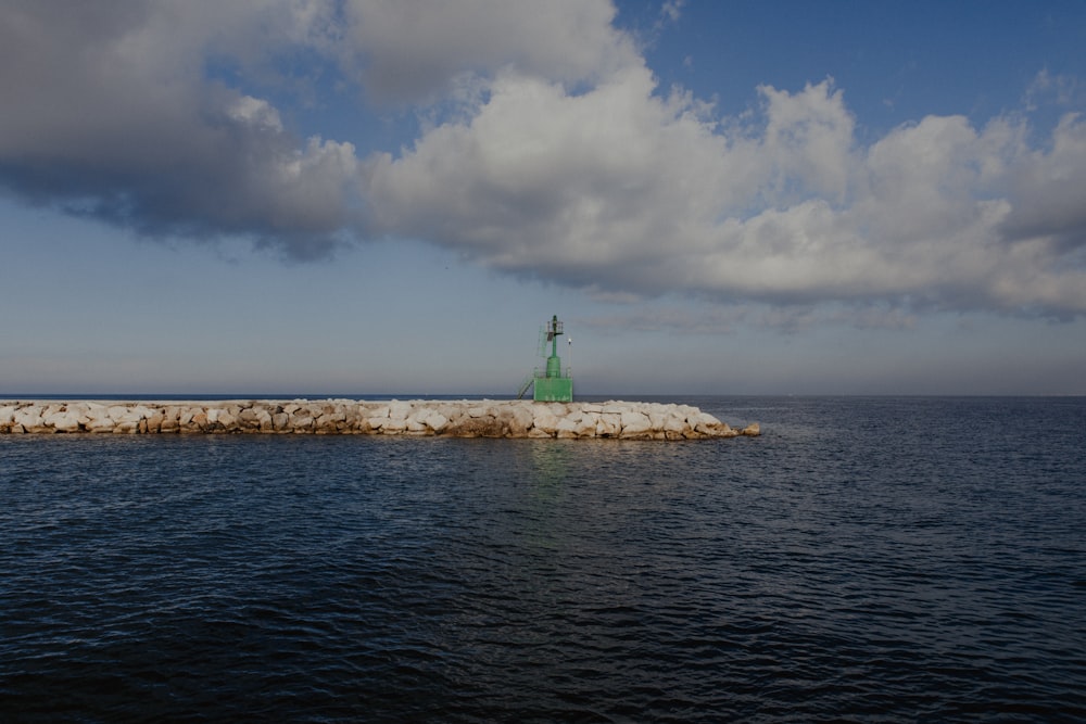 a green lighthouse on a rock outcropping in the middle of the ocean