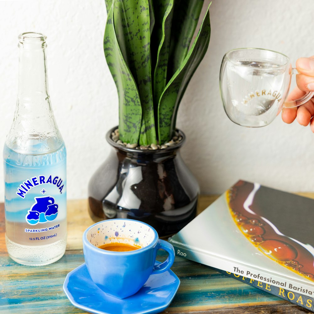 una persona sosteniendo una taza de café junto a una botella de agua