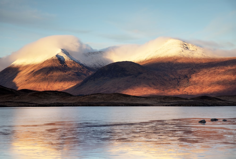 a mountain covered in snow next to a body of water