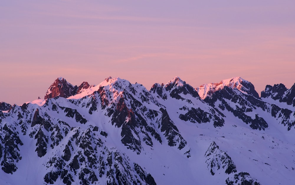 a mountain range covered in snow at sunset