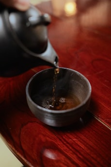 a person pouring tea into a bowl on a wooden table