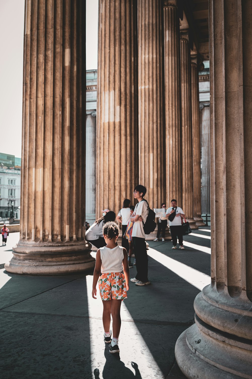a little girl standing in front of some large pillars