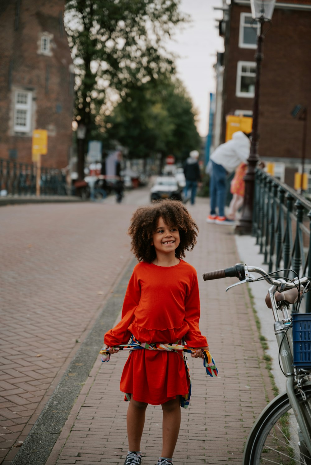 a little girl standing next to a bike on a sidewalk