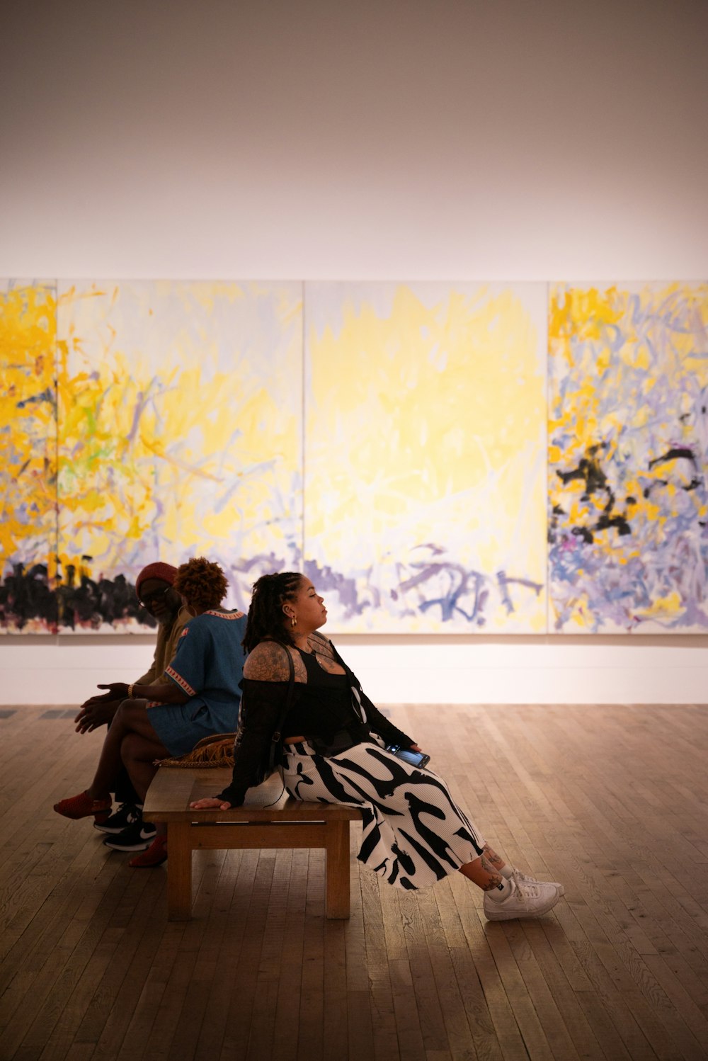 two women sitting on a bench in front of a painting