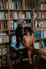 a man and a woman sitting on a chair in front of a bookshelf