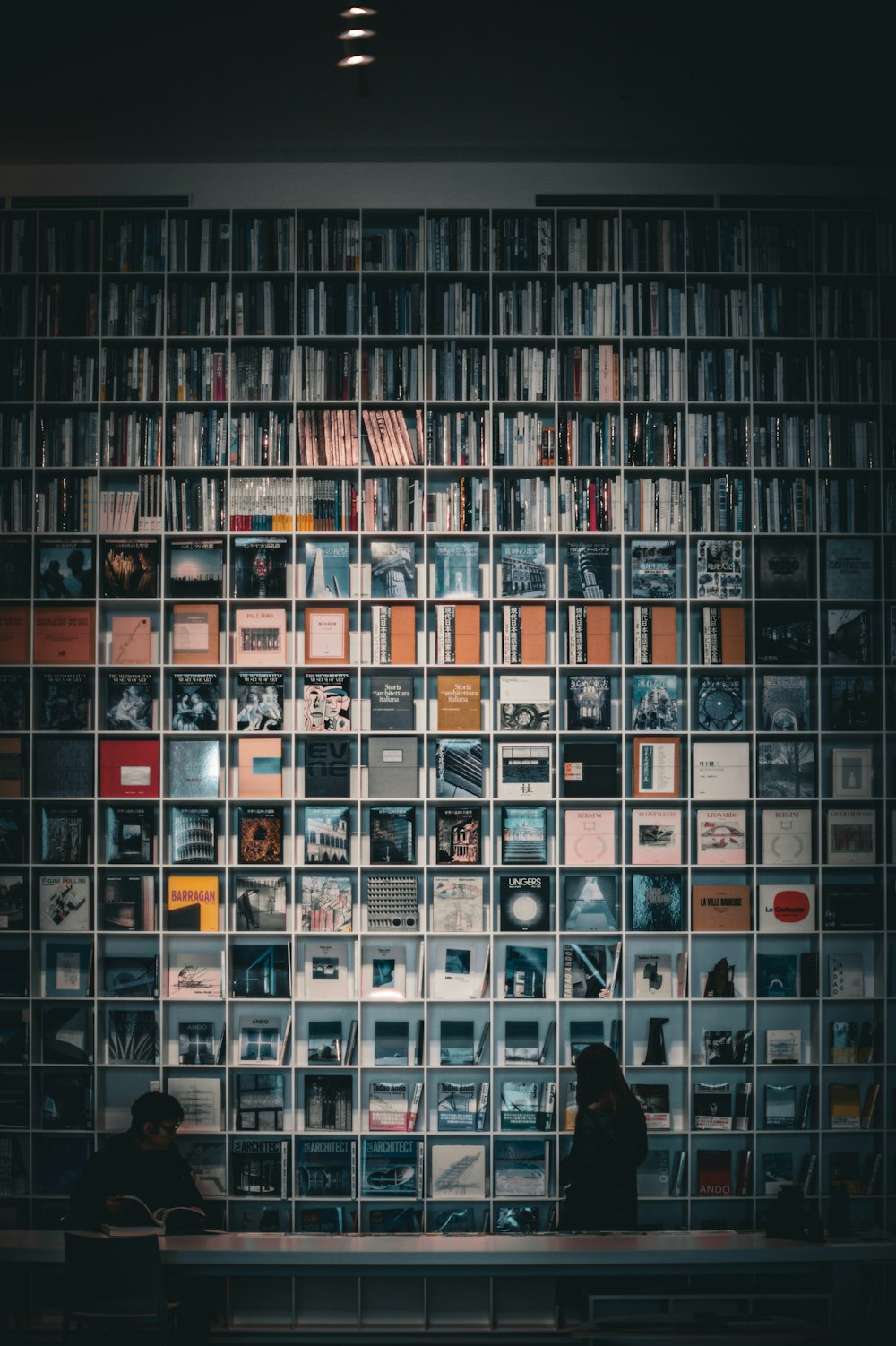 two people sitting on a bench in front of a wall of books