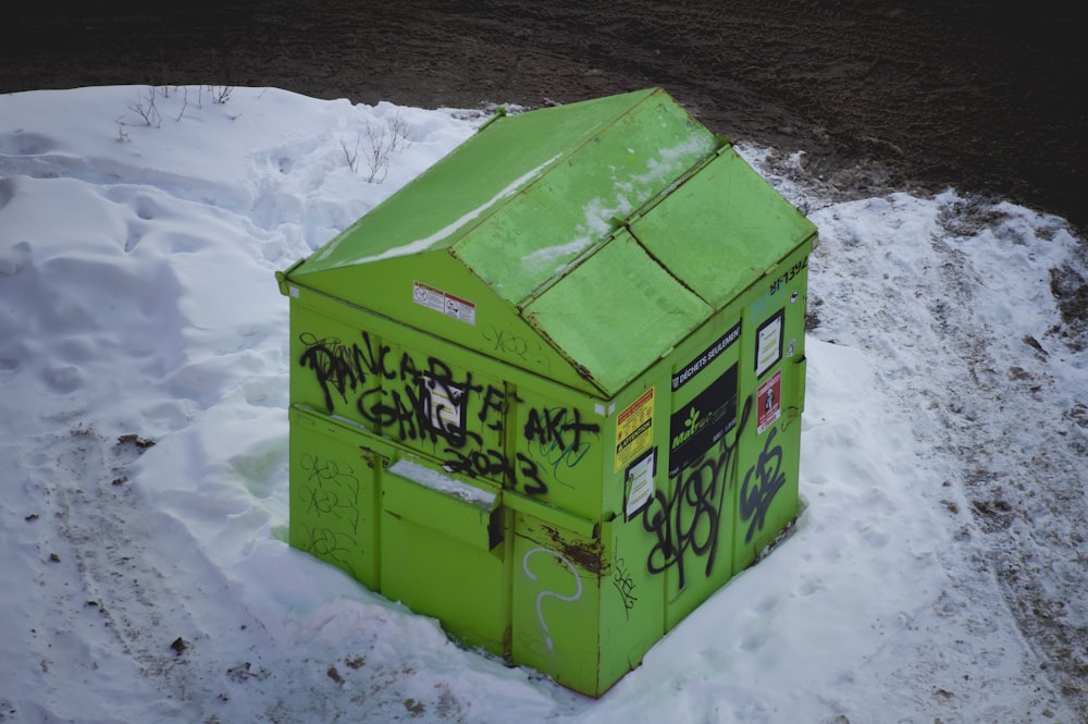una caja verde cubierta de grafitis en la nieve
