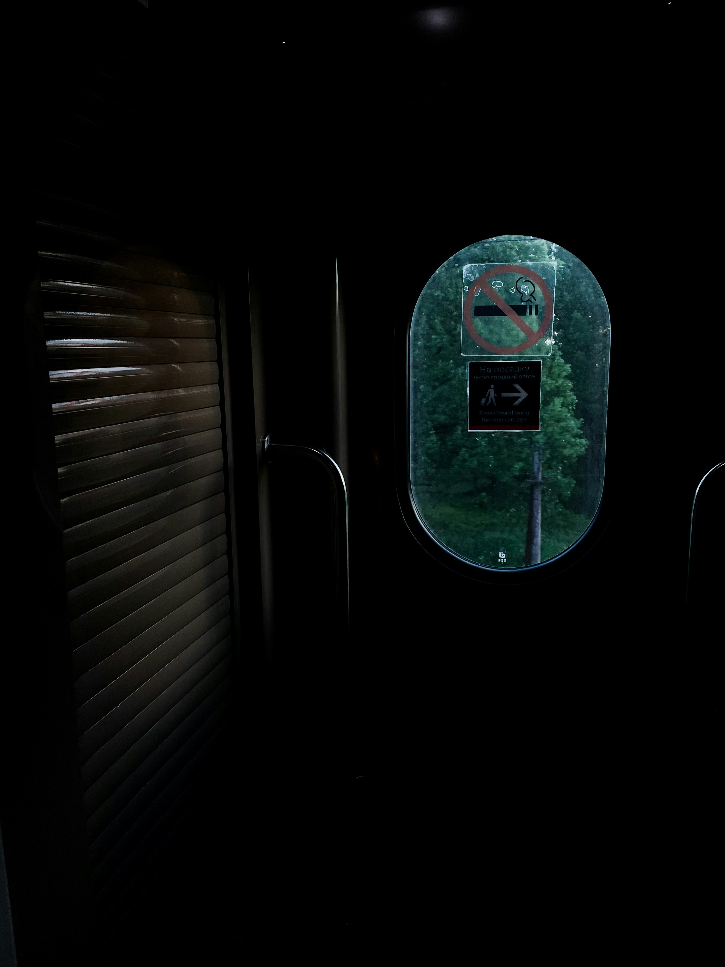 Inside a dark train cabin, a window shows the outdoors.